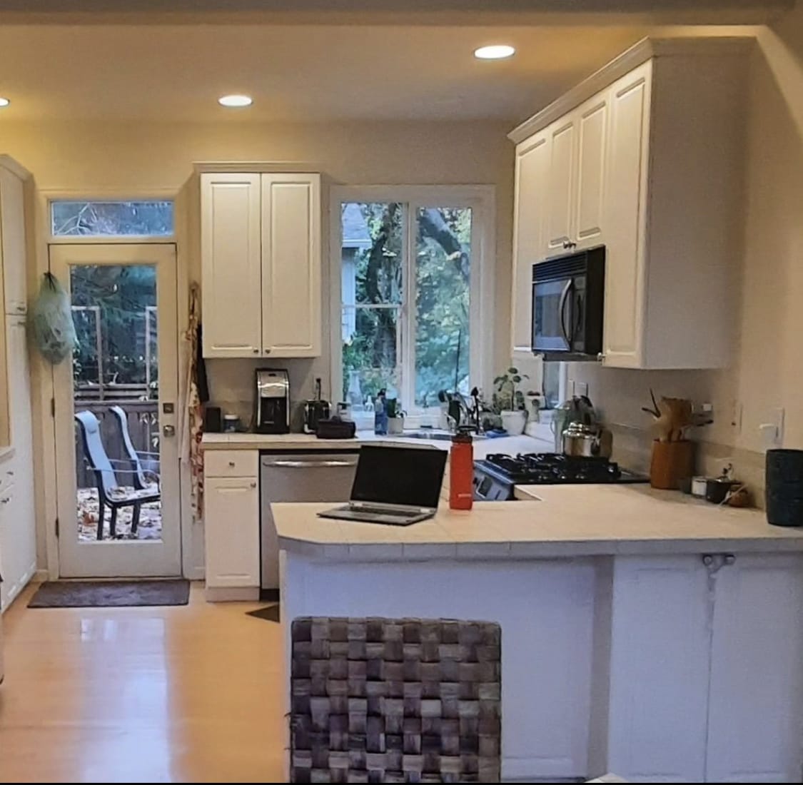 Before the remodel: dated white cabinets, tile counters, and a black over-range microwave in an Ashcreek kitchen, SW Portland — K&H Construction