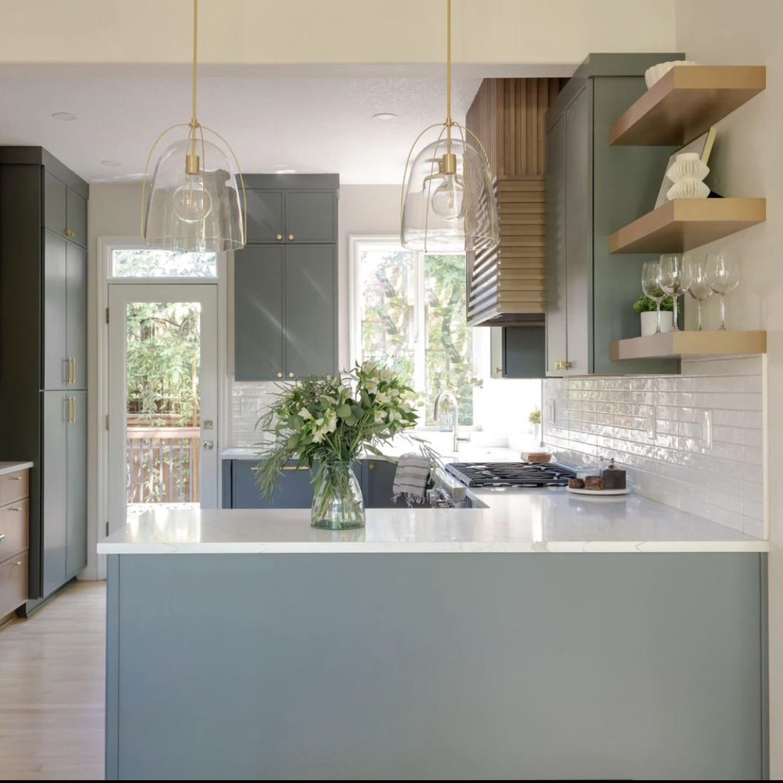 Compact Portland kitchen remodel with sage green peninsula, glass pendant lights, and white tile backsplash by K&H Construction