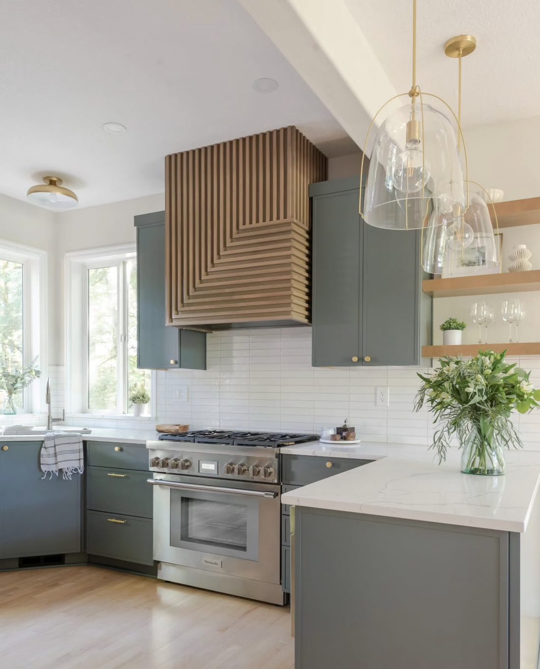 Sage green kitchen cabinets with custom fluted white oak range hood and brass hardware in a Portland home